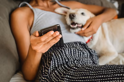 Tutora no sofá agendando consulta pelo celular com o cachorro